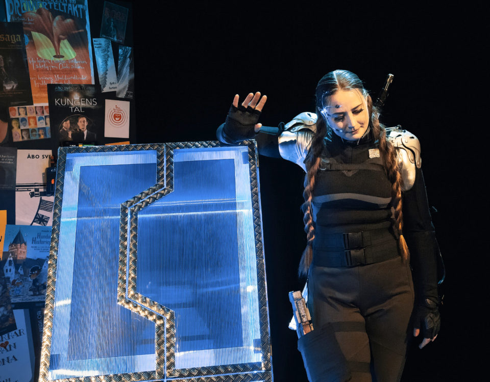 Kvinna med långa flätor står bredvid futuristisk blåskimrande låda i plast och metall.
