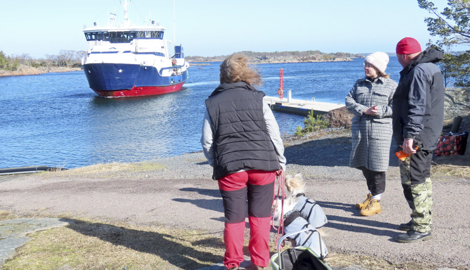 Tre personer på en kaj. En förbindelsebåt på väg.