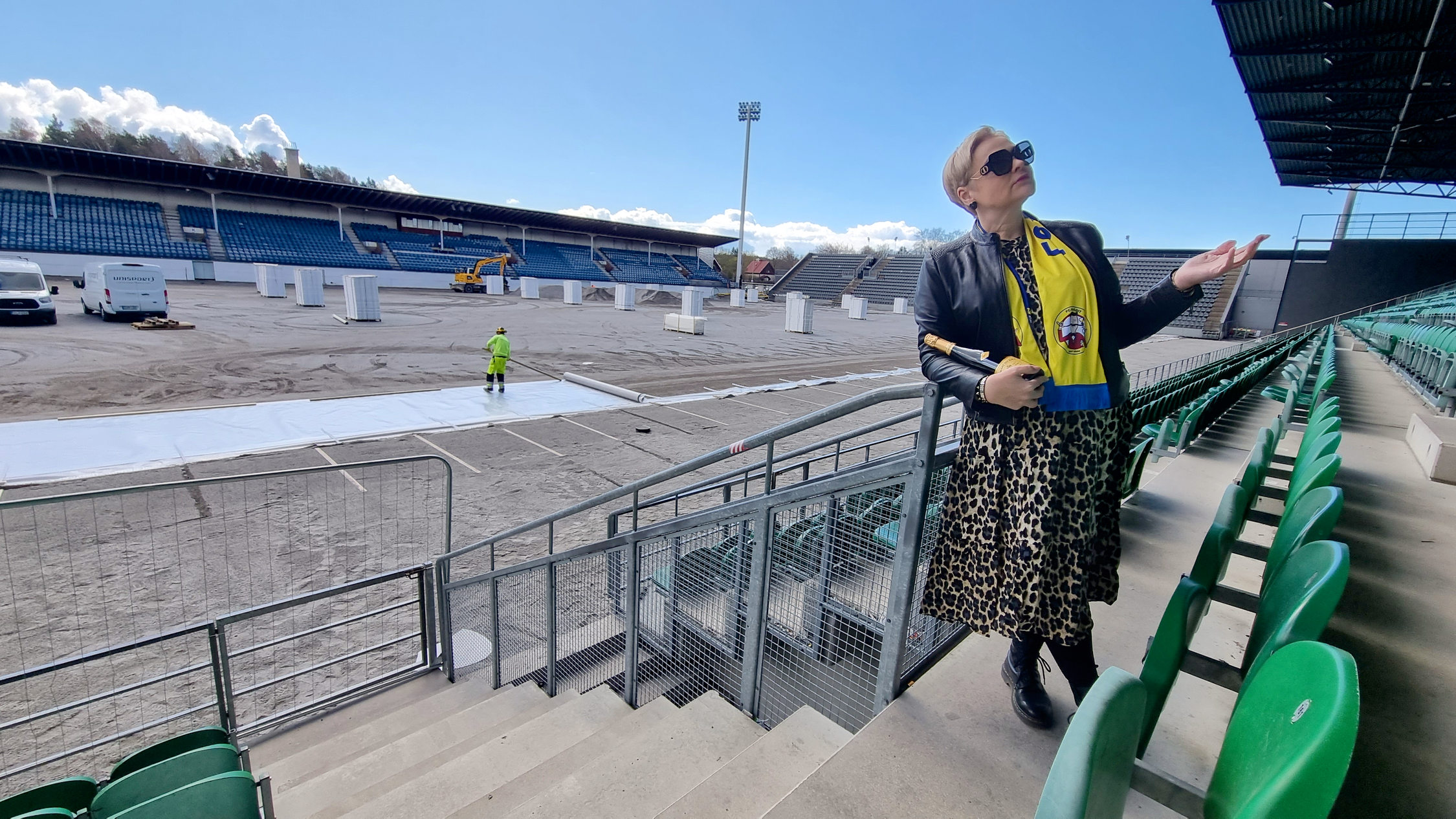 Kvinna på läktare vid fotbollsplan där arbete pågår.