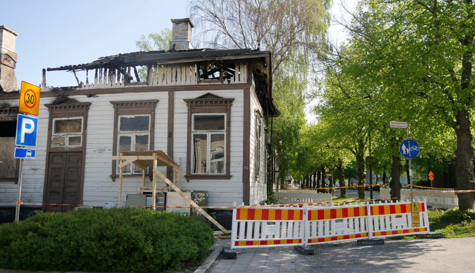 Trähus med skador av brand, staket runt.