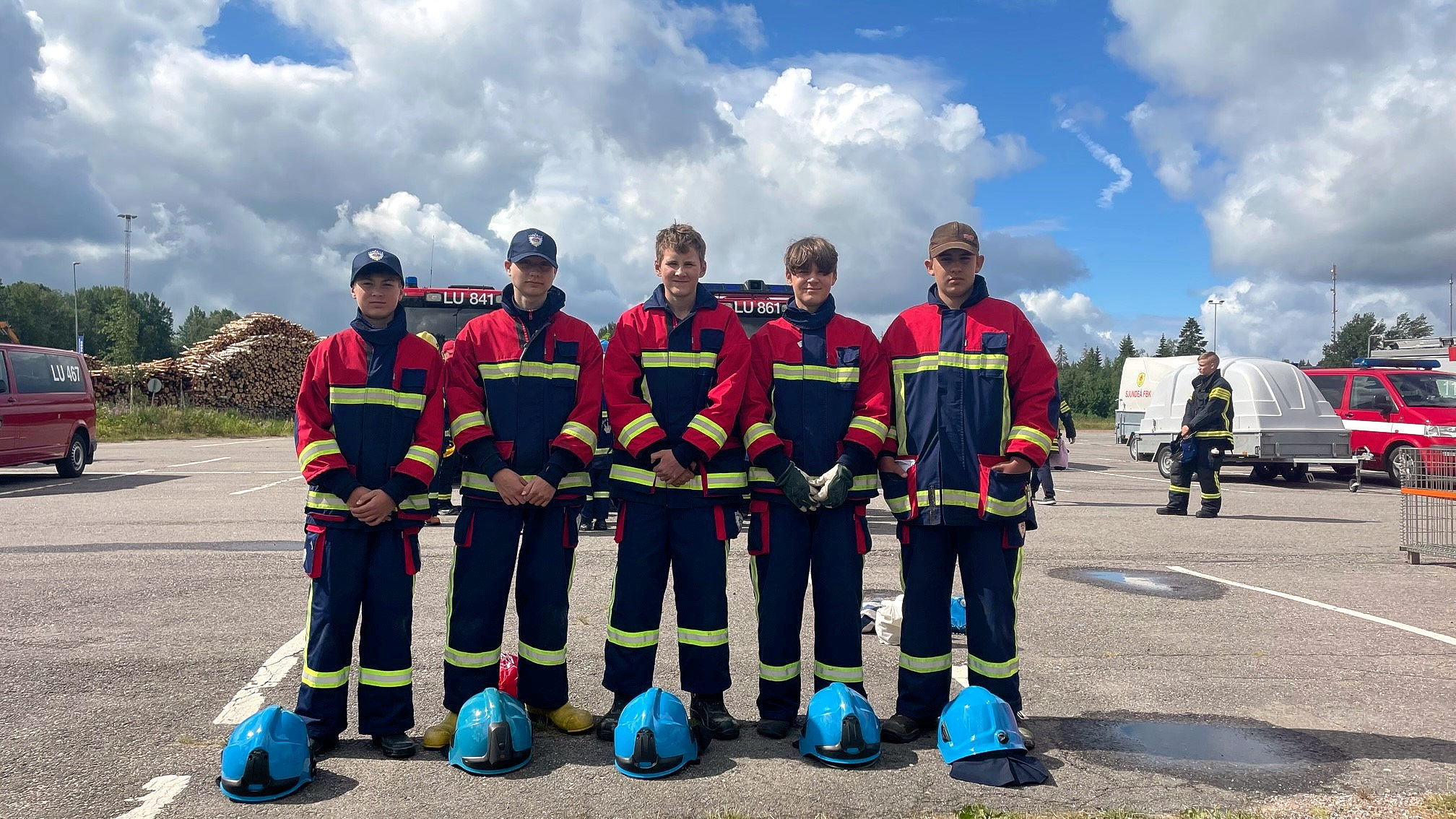 Fem unga pojkar som står utomhus i brandmansutrustning.