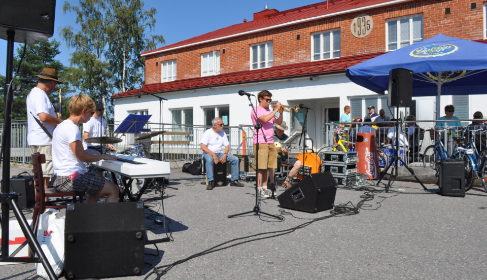 Musiker som spelar utomhus på ett torg. I bakgrunden ett tvåvåningshus i sten och tegel.