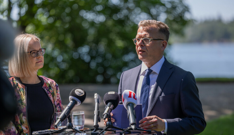 En kvinna och en man står vid ett bord med mediernas mikrofoner i parkmiljö.