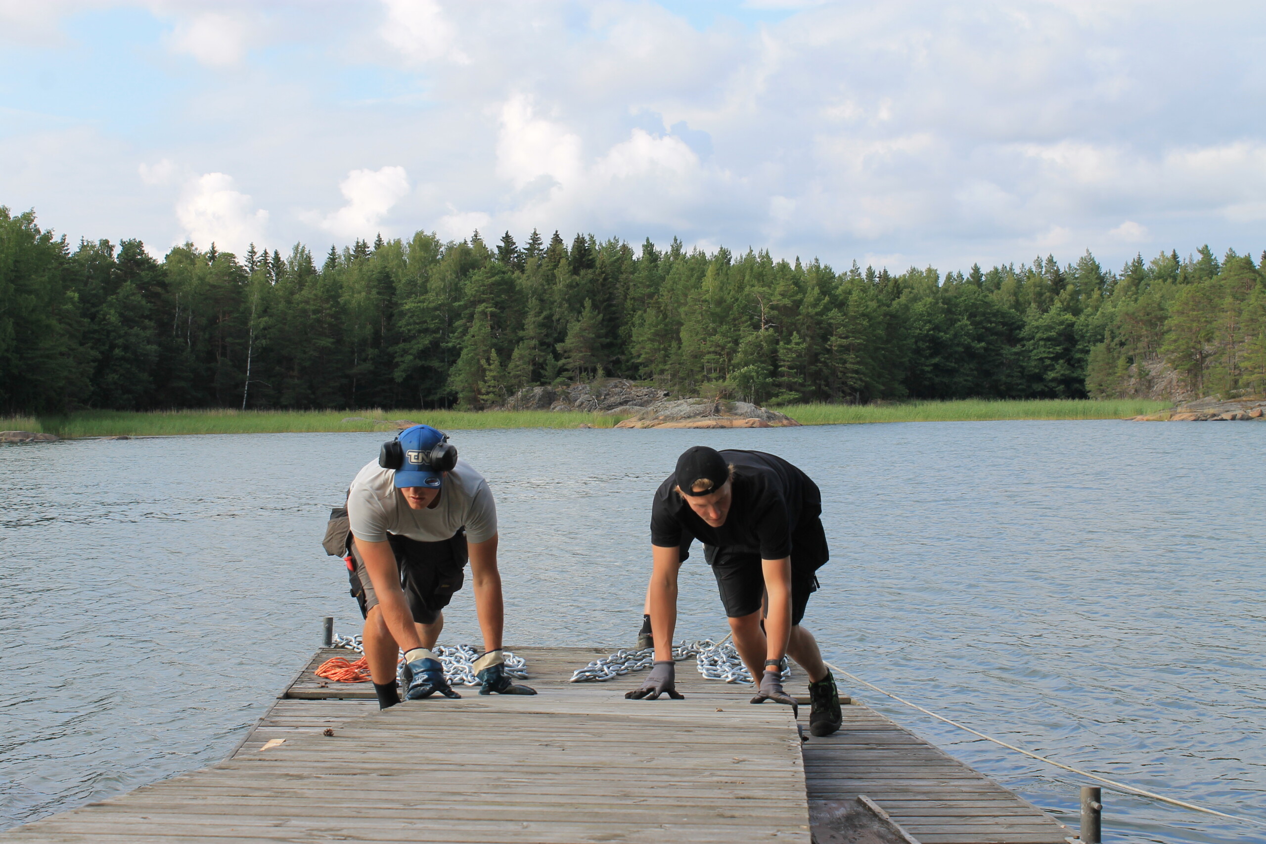 Två unga män som arbetar på en brygga. I bakgrunden Ekenäs skärgård.