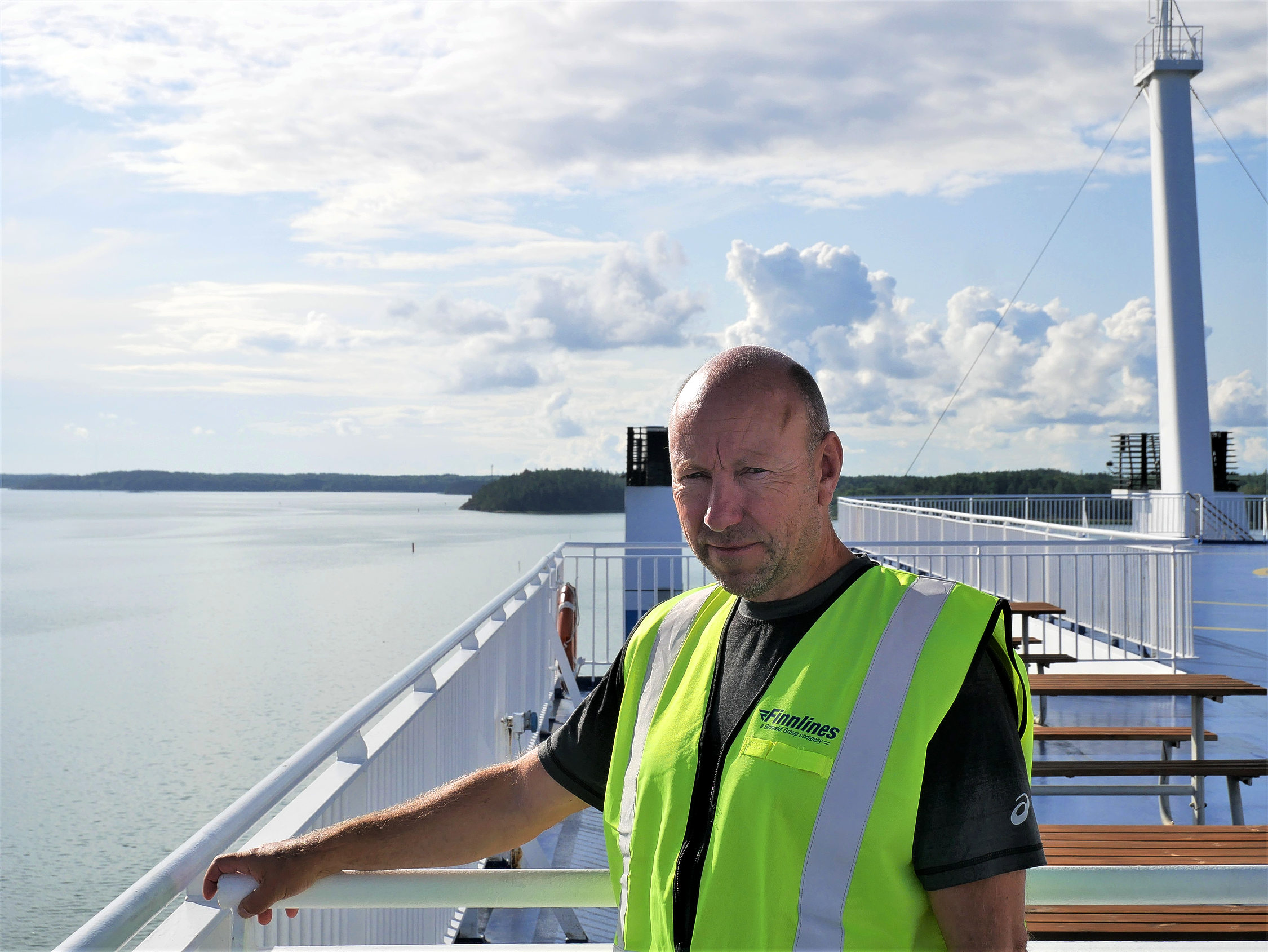 En man i reflexväst står på en fartyg med havet i bakgrunden.