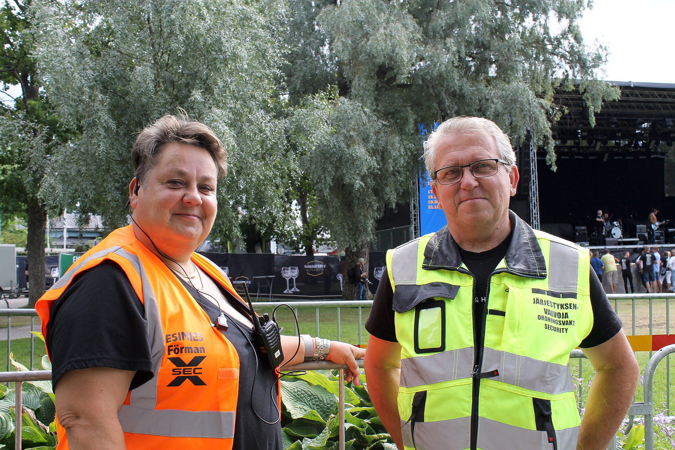 En man och en kvinna står bredvid varandra, de bär reflexvästar och arbetar som ordningsvakter på Rasebrogfestivalen i Stallörs parken i Ekenäs.