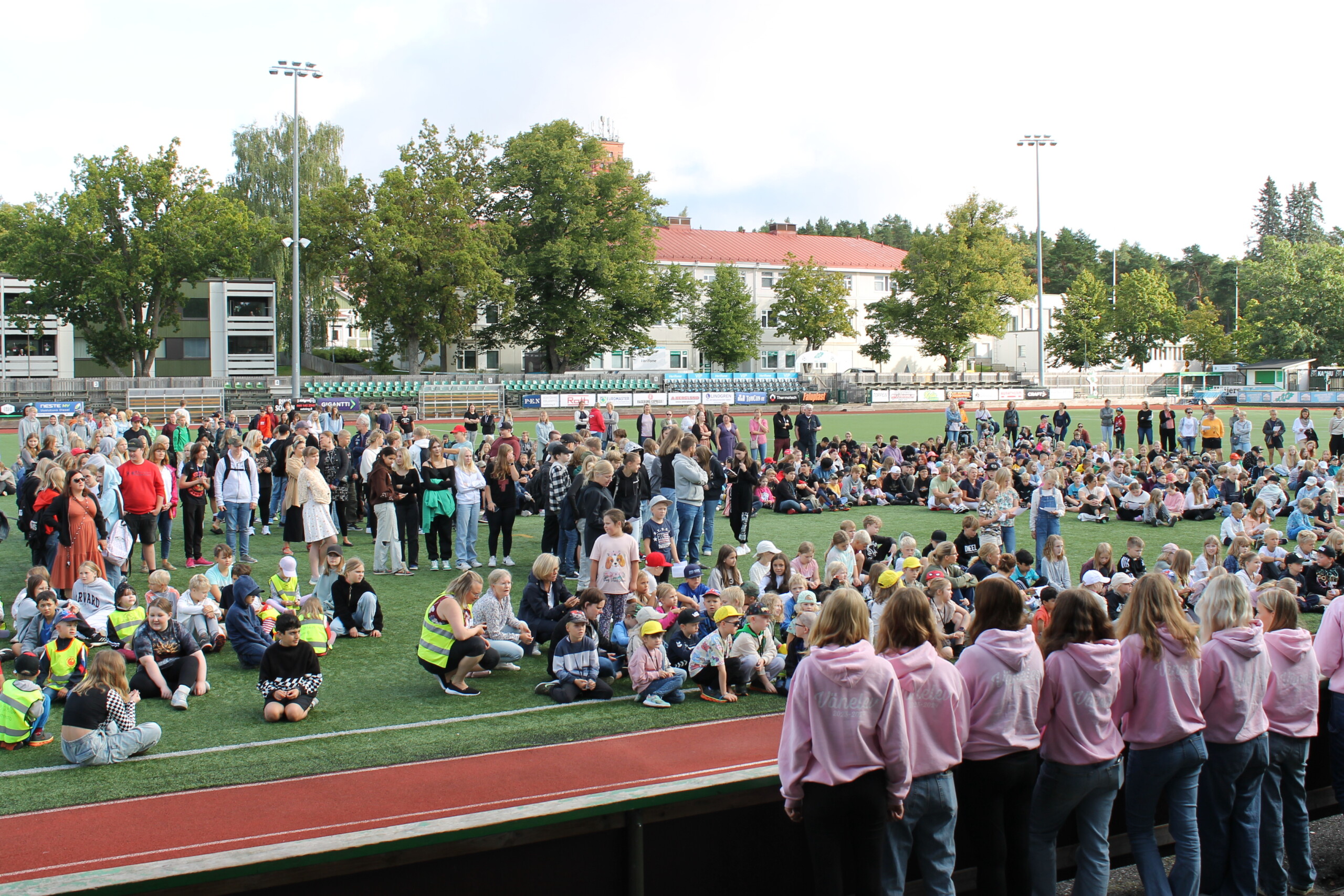 Centrumplan i Ekenäs. Elever från tre olika skolor har samlats utomhus för att utlysa skolfreden. Många elever i olika åldrar är på planen och vid staketet runt planen står några vänelever med ryggen mot kameran och blickar ut över samlingen människor.