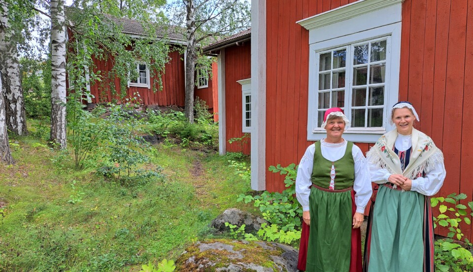 Två kvinnor i folkdräkter utomhus framför ett rött hus.