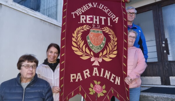 tre kvinnor och en man står vid en purpurröd flagga