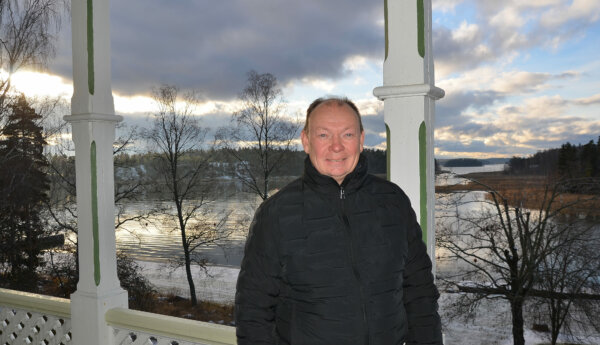 en tunnhårig man står på en veranda med ett vintrigt skärgårdslandskap i bakgrunden